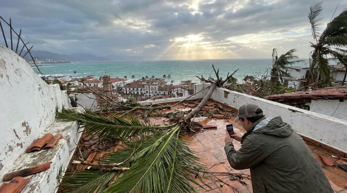 La mañana después de un huracán en Puerto Vallarta: un propietario fotografía los daños en la terraza de una casa en la ladera cubierta de hojas de palma caídas, con la Bahía de Banderas al fondo